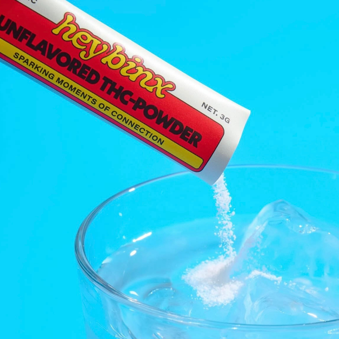 Unflavored THC powder being poured from a 'hey binx' container into a glass against a blue background.